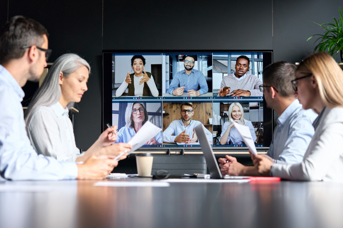 a business meeting with half of the employees engaging in the conversation through a video call.