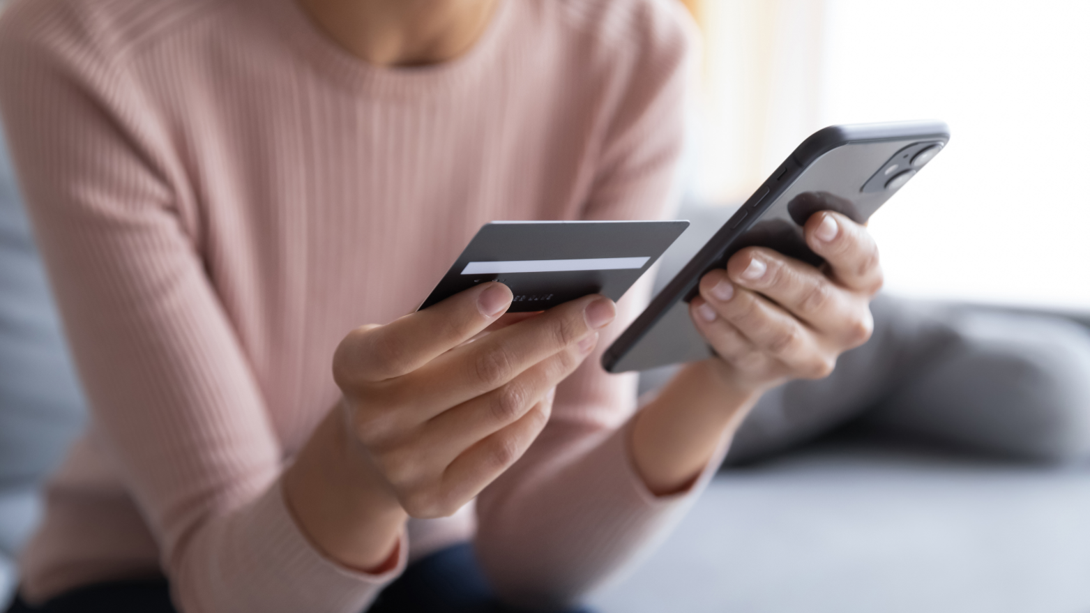 A woman looking at her credit card and her phone, completing a financial transaction online.