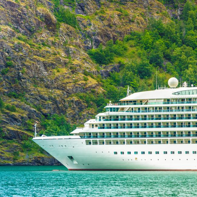 Cruise ship in the water with the backdrop of a mountain covered in green grass.