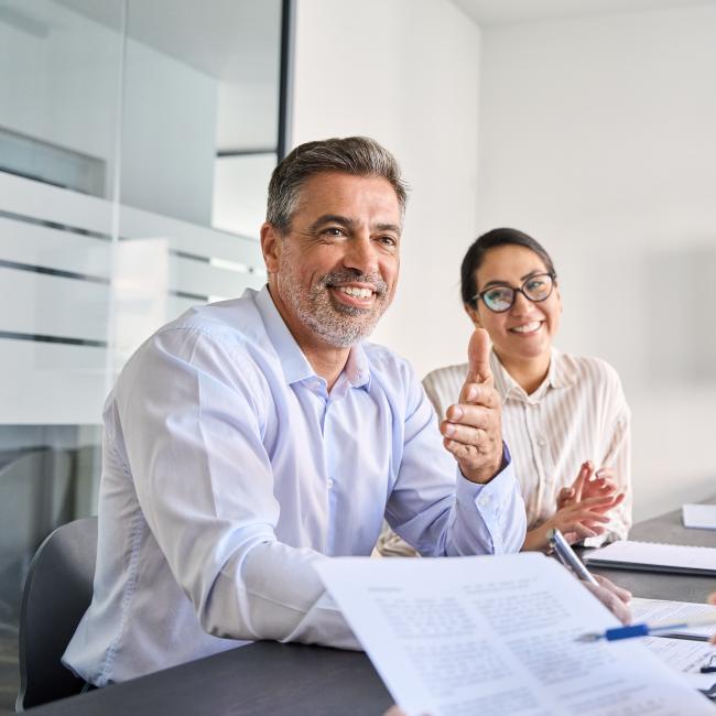 A professional translator and banker smiling and chatting with a client at a desk. 