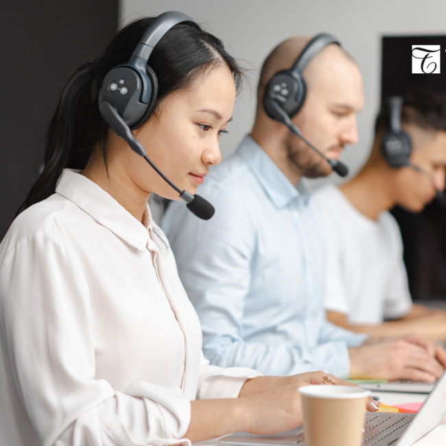Three sales people with headsets, sitting side-by-side while typing on their laptops. 