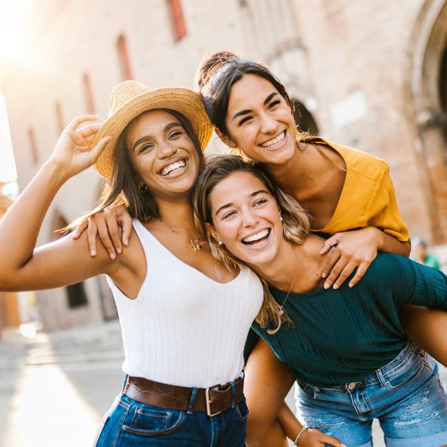 Three friends smiling posing for a picture in front of an older building while traveling..