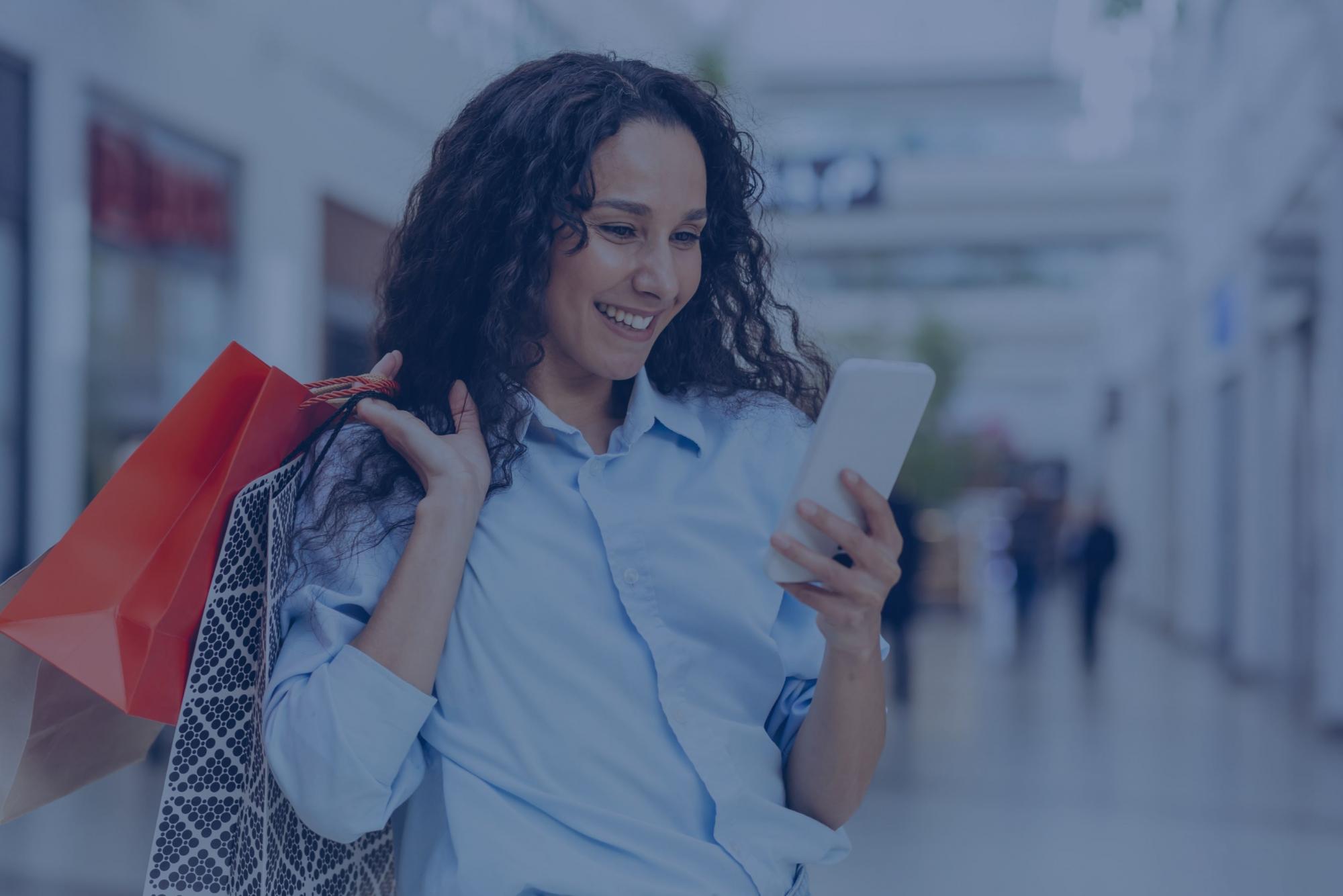 A woman looks at her phone while holding shopping bags.