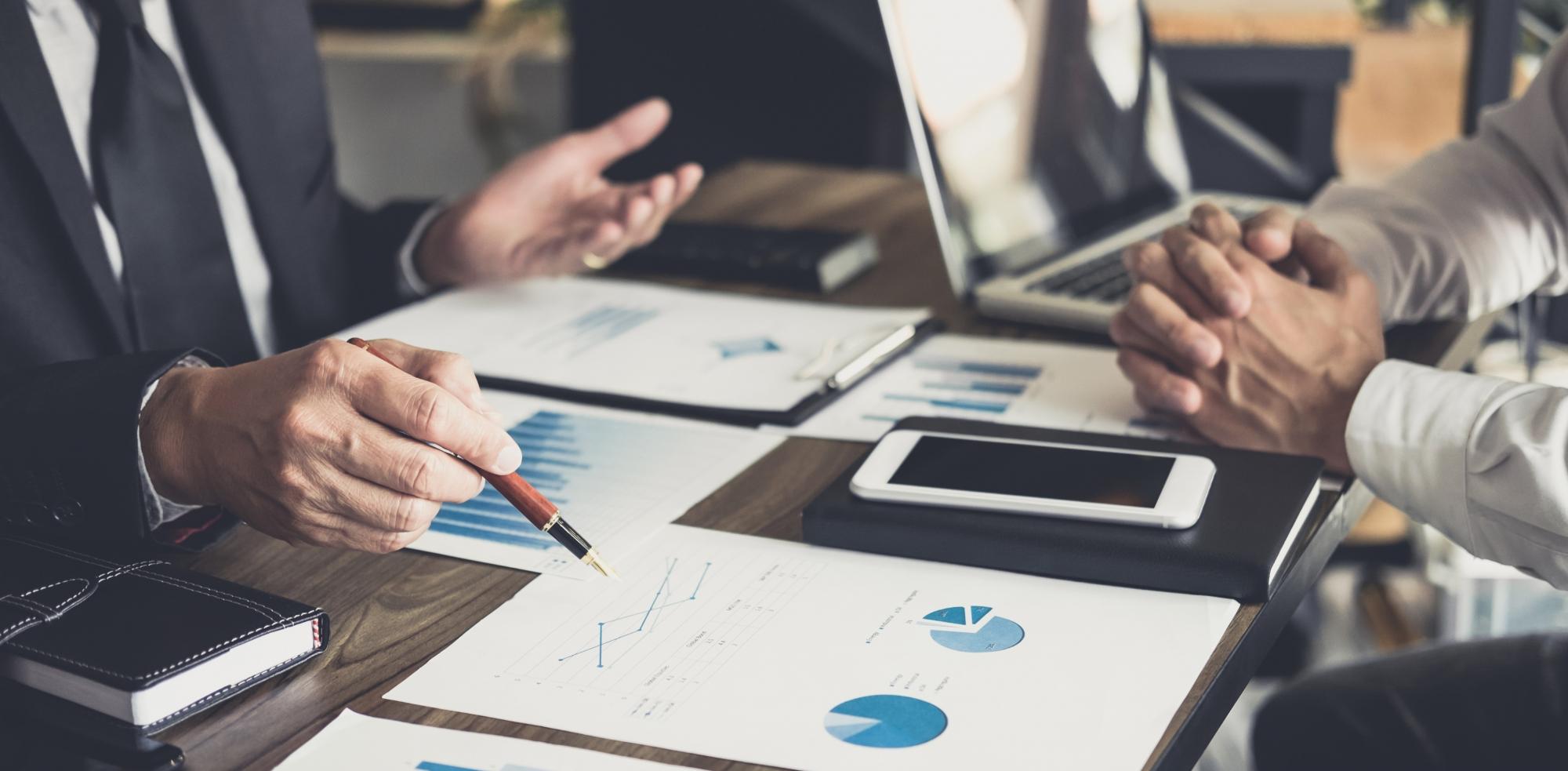 Financial expert pointing at a graph while sitting across from a colleague.