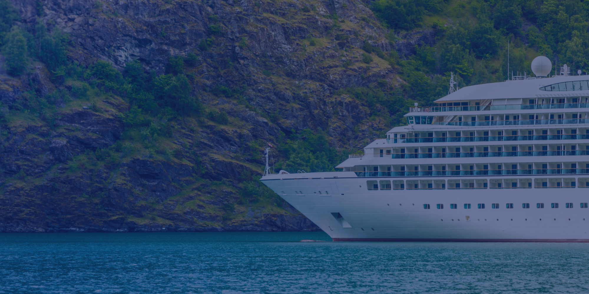 Cruise ship in the water with the backdrop of a mountain covered in green grass.