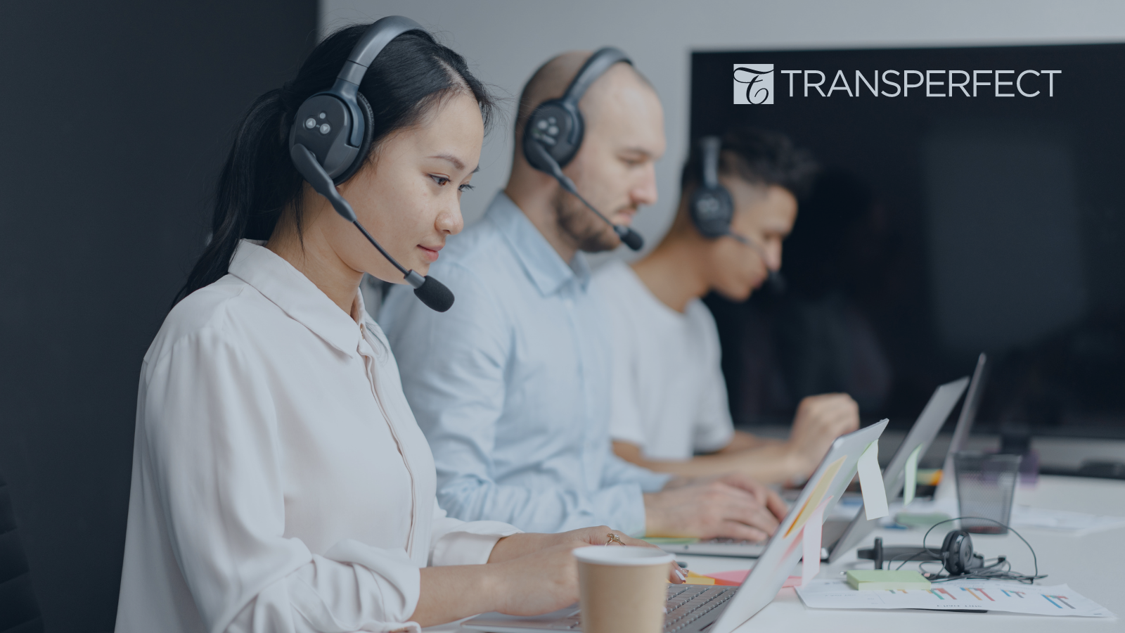 Three sales people with headsets, sitting side-by-side while typing on their laptops.