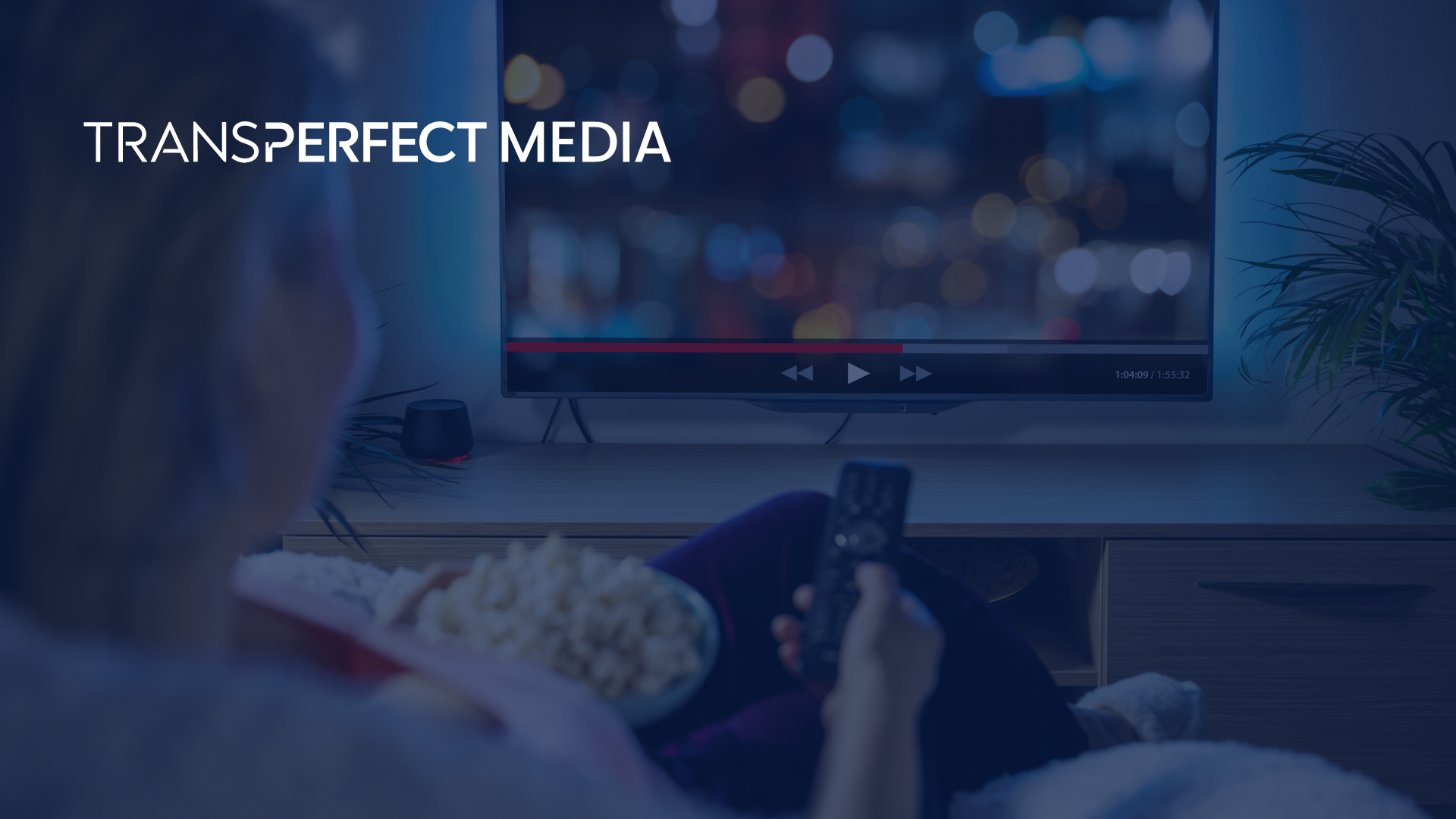 A woman sits on her couch with popcorn and a tv remote pointed at her tv while she pauses/plays a film playing.