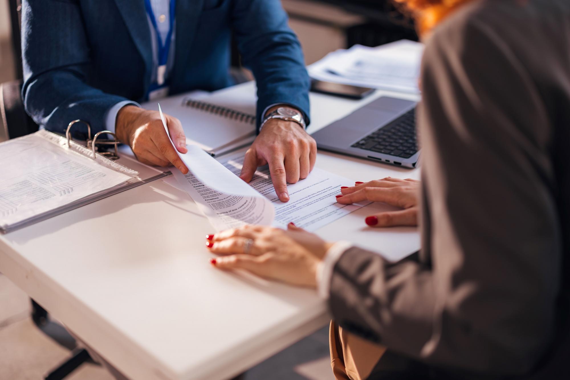 A banker and a client sitting opposite each other at a desk reviewing a document.