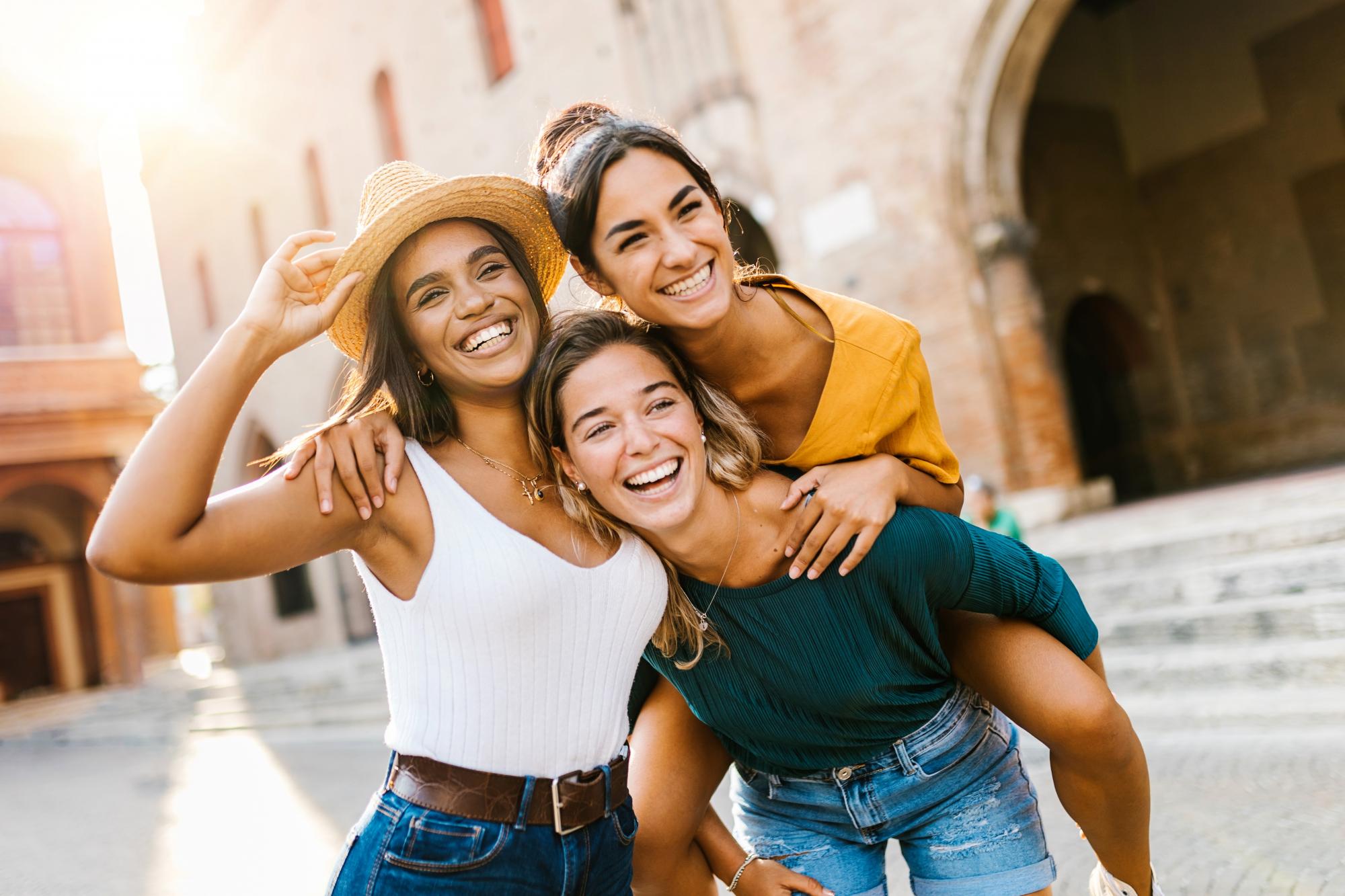 Three friends smiling posing for a picture in front of an older building while traveling..